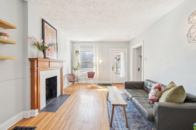 living room with visible vents, baseboards, a tiled fireplace, hardwood / wood-style flooring, and a textured ceiling