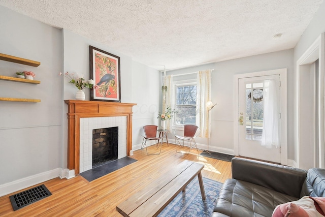 living area with a tiled fireplace, visible vents, baseboards, and wood finished floors