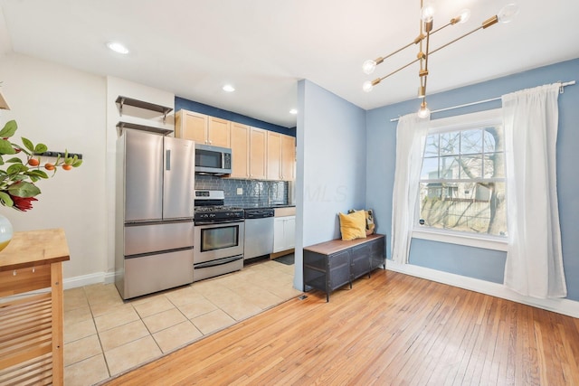 kitchen with tasteful backsplash, baseboards, light wood-type flooring, hanging light fixtures, and stainless steel appliances