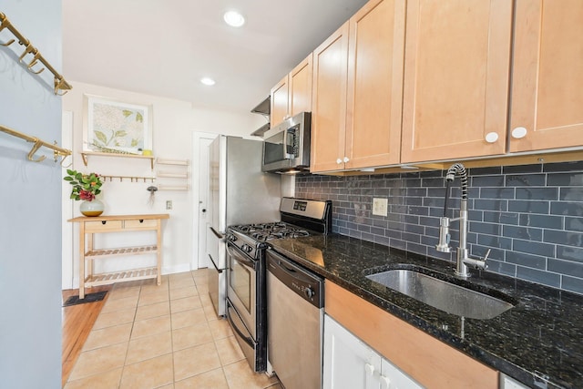 kitchen featuring a sink, dark stone countertops, backsplash, stainless steel appliances, and light tile patterned floors