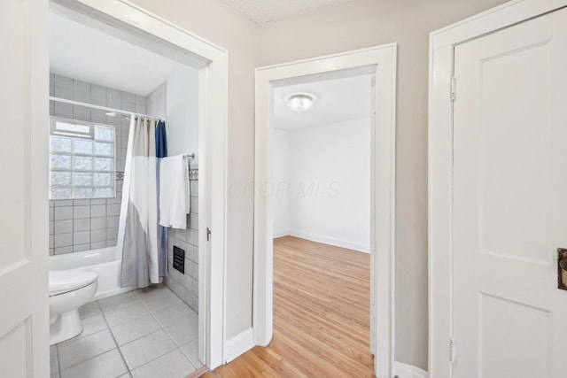 bathroom featuring tile patterned floors, baseboards, toilet, and shower / bath combo