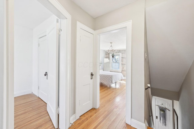 hall with baseboards, an inviting chandelier, and light wood-style flooring