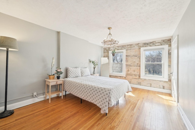 bedroom with a chandelier, baseboards, a textured ceiling, and light wood-style floors