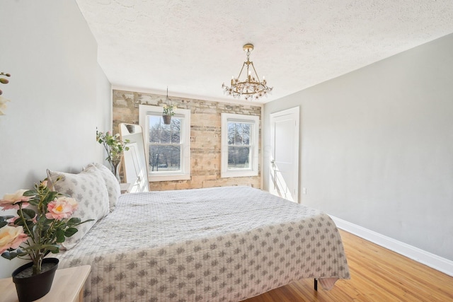 bedroom featuring a chandelier, a textured ceiling, baseboards, and wood finished floors