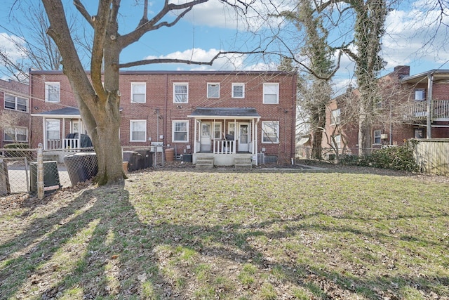 rear view of house featuring fence, brick siding, and a lawn