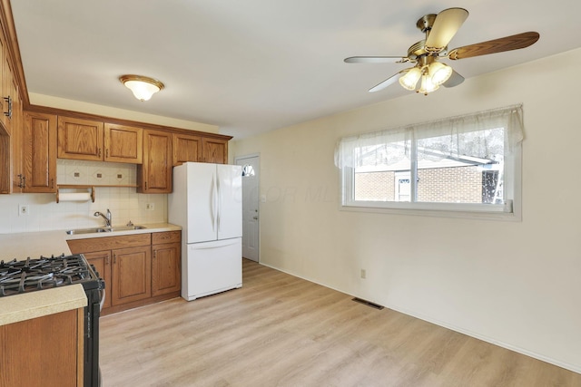 kitchen with sink, black range with gas stovetop, decorative backsplash, white fridge, and light hardwood / wood-style flooring