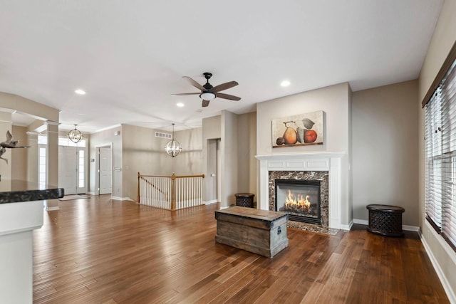 unfurnished living room featuring hardwood / wood-style flooring, a high end fireplace, ceiling fan with notable chandelier, and decorative columns