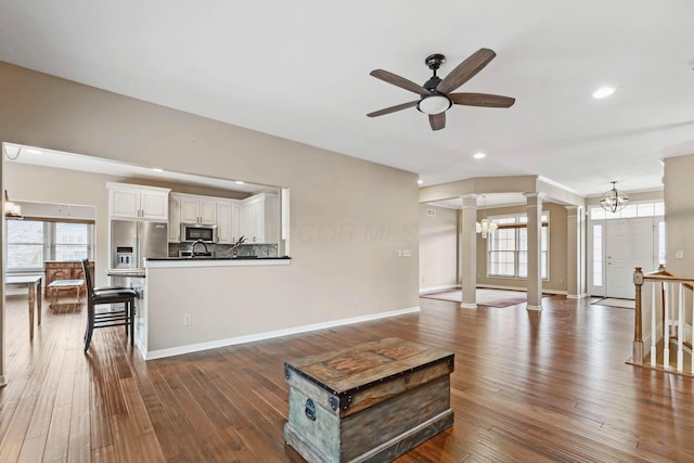 living room featuring ceiling fan with notable chandelier, decorative columns, and dark hardwood / wood-style floors