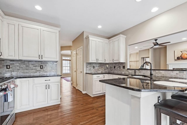 kitchen with sink, stainless steel gas range, a breakfast bar, white cabinetry, and dark stone counters