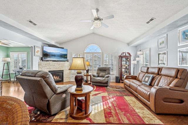 living room with wood-type flooring, vaulted ceiling, a textured ceiling, ceiling fan, and a fireplace