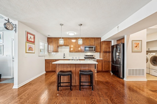 kitchen with stainless steel appliances, washer and dryer, a kitchen island, dark hardwood / wood-style flooring, and decorative light fixtures