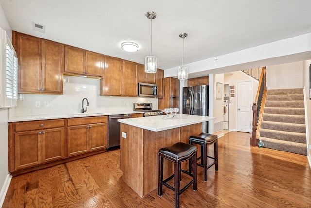 kitchen with appliances with stainless steel finishes, pendant lighting, washer / clothes dryer, sink, and a center island