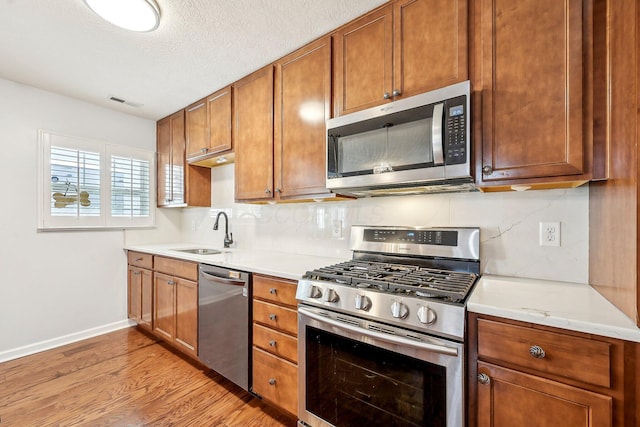 kitchen featuring sink, stainless steel appliances, tasteful backsplash, light hardwood / wood-style floors, and a textured ceiling