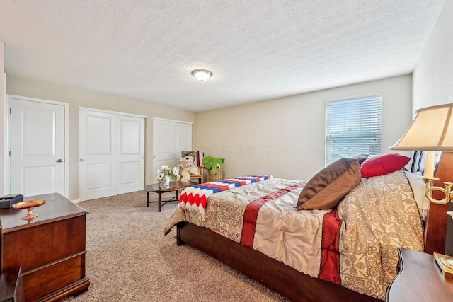 bedroom with a textured ceiling, carpet, and two closets