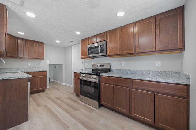 kitchen featuring light stone countertops, appliances with stainless steel finishes, a textured ceiling, and light hardwood / wood-style floors