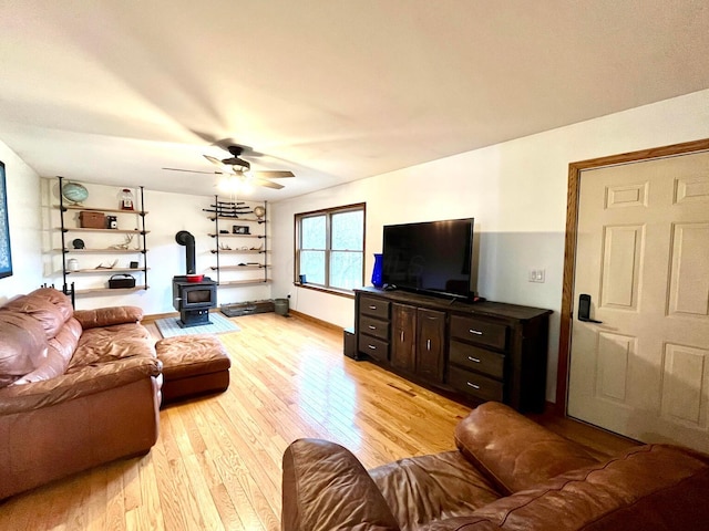 living room featuring ceiling fan, light hardwood / wood-style floors, and a wood stove