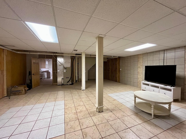 basement featuring a paneled ceiling, heating unit, and light tile patterned floors