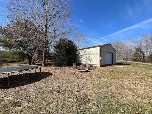 view of yard with a garage, an outbuilding, a trampoline, and a fire pit