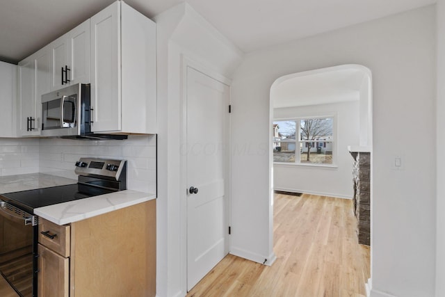 kitchen featuring appliances with stainless steel finishes, tasteful backsplash, white cabinets, light stone countertops, and light hardwood / wood-style flooring