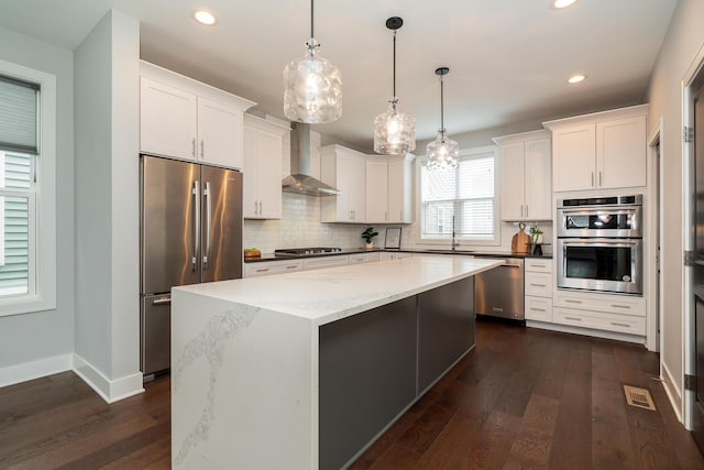 kitchen with pendant lighting, sink, appliances with stainless steel finishes, a kitchen island, and wall chimney exhaust hood