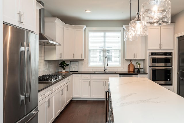 kitchen featuring wall chimney exhaust hood, sink, white cabinetry, decorative light fixtures, and appliances with stainless steel finishes