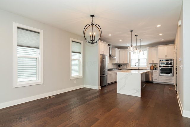 kitchen featuring sink, decorative light fixtures, a center island, stainless steel appliances, and light stone countertops