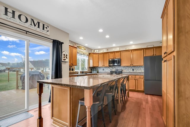 kitchen featuring backsplash, a kitchen bar, stainless steel appliances, a kitchen island, and light wood-type flooring