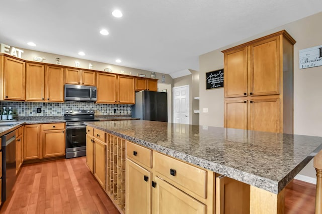 kitchen with backsplash, a kitchen island, dark stone counters, and appliances with stainless steel finishes