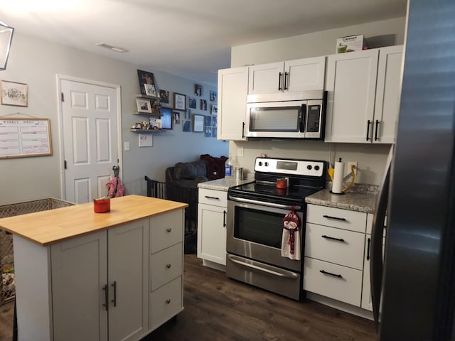 kitchen featuring dark wood-type flooring, butcher block counters, appliances with stainless steel finishes, a kitchen island, and white cabinets