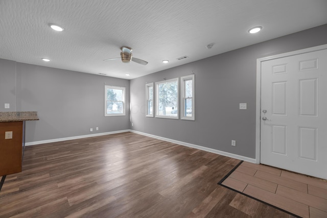 unfurnished living room with a textured ceiling, dark wood-type flooring, and ceiling fan