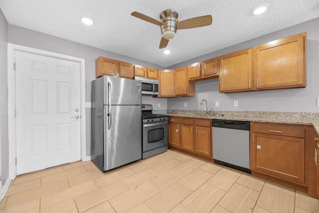 kitchen with ceiling fan, appliances with stainless steel finishes, sink, and light stone counters