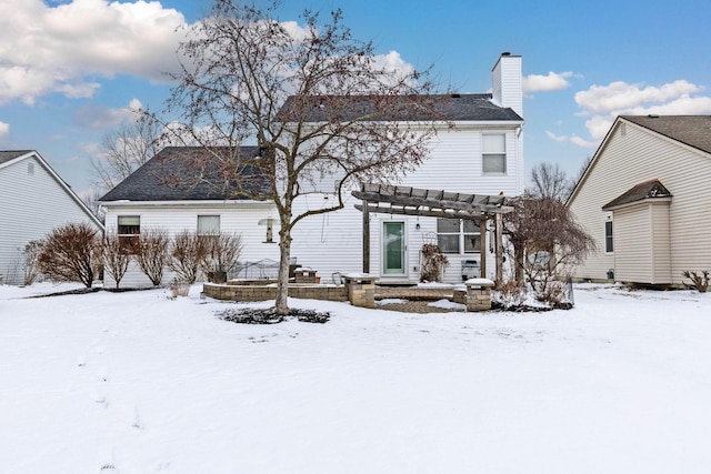 snow covered rear of property with a chimney and a pergola