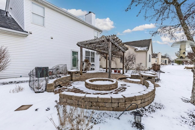 snow covered house with a fire pit, a chimney, and a pergola