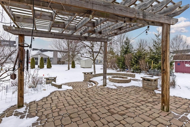 snow covered patio featuring a shed, a fire pit, a pergola, and an outdoor structure