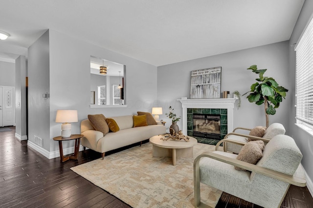 living room featuring dark wood-style floors, visible vents, a tiled fireplace, and baseboards