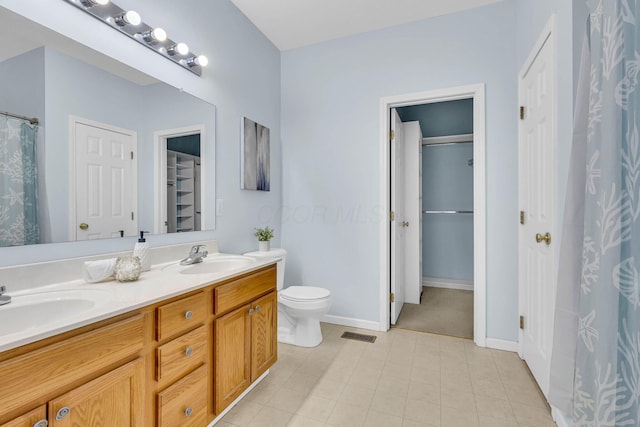 full bath with double vanity, visible vents, a walk in closet, and a sink