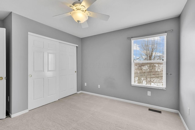 unfurnished bedroom featuring ceiling fan, light carpet, visible vents, baseboards, and a closet