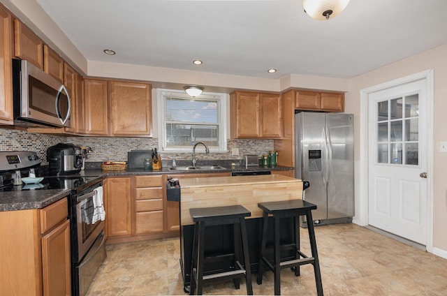 kitchen featuring stainless steel appliances, dark countertops, backsplash, brown cabinetry, and a sink