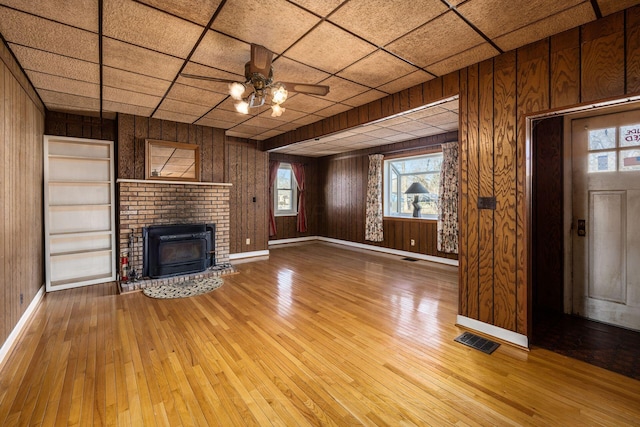 unfurnished living room featuring wooden walls, a fireplace, visible vents, and light wood-style floors