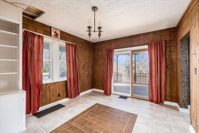 entryway with a textured ceiling, plenty of natural light, visible vents, and wooden walls