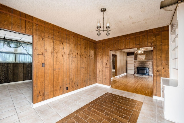 unfurnished dining area with a textured ceiling, tile patterned flooring, wood walls, a fireplace, and a ceiling fan