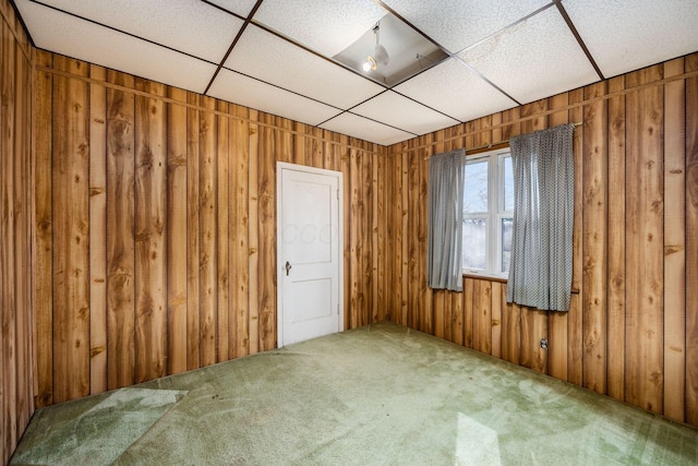 carpeted spare room with a paneled ceiling and wooden walls