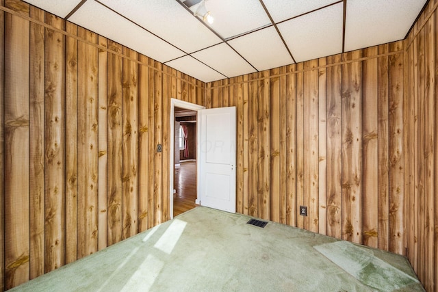 carpeted empty room with visible vents and wooden walls