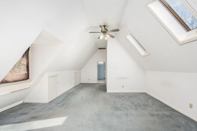 additional living space with carpet floors, vaulted ceiling with skylight, a ceiling fan, and baseboards