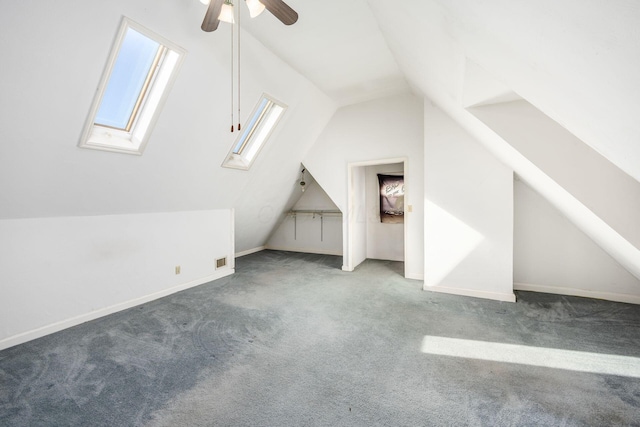 bonus room featuring a ceiling fan, dark colored carpet, visible vents, and vaulted ceiling with skylight