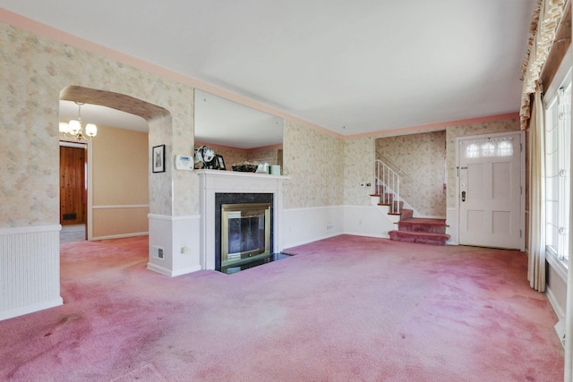 unfurnished living room with wallpapered walls, stairs, a fireplace, and wainscoting