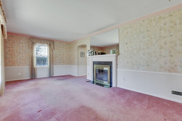 unfurnished living room with a fireplace with flush hearth, wainscoting, wallpapered walls, and carpet