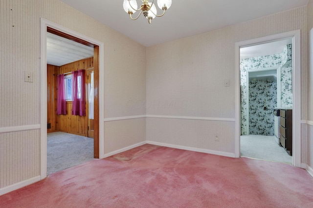 spare room with baseboards, a notable chandelier, carpet flooring, and wallpapered walls