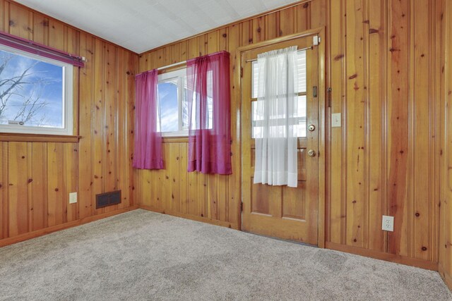 unfurnished room with visible vents, wood walls, and carpet flooring