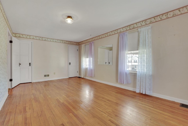 unfurnished room with light wood-style floors, visible vents, and baseboards